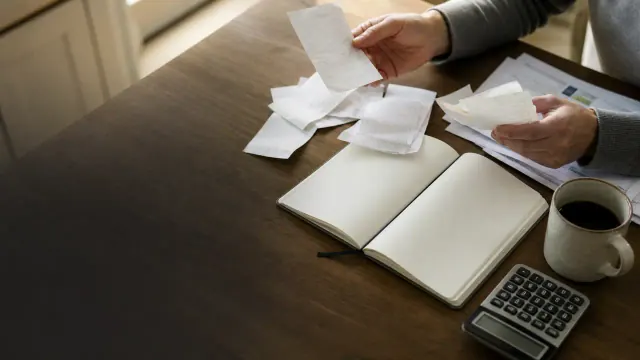 Hands sorting receipts beside a notebook and calculator